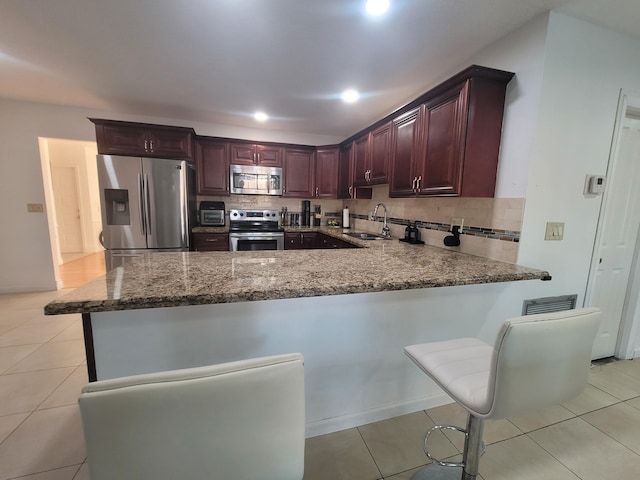 kitchen featuring sink, a kitchen breakfast bar, kitchen peninsula, stainless steel appliances, and decorative backsplash