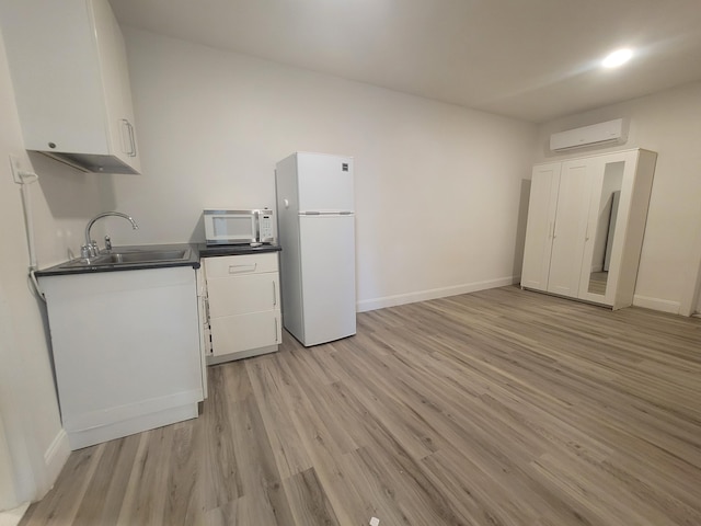 kitchen featuring sink, light wood-type flooring, an AC wall unit, white appliances, and white cabinets