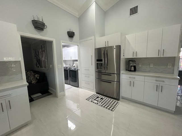 kitchen featuring stainless steel refrigerator with ice dispenser, washing machine and clothes dryer, ornamental molding, a high ceiling, and backsplash