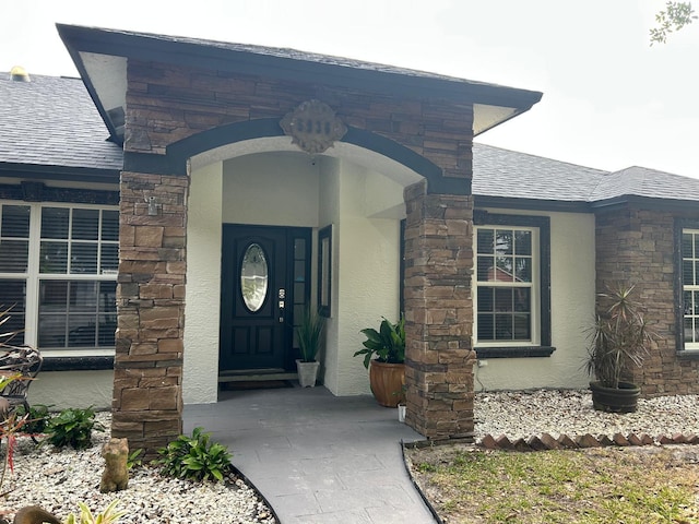 entrance to property featuring stucco siding, stone siding, and a shingled roof