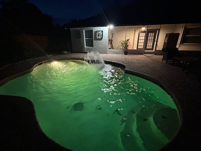 pool at night with french doors and a patio area