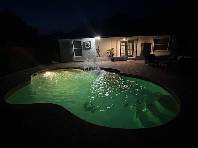 pool at night with a patio, french doors, and an outdoor pool