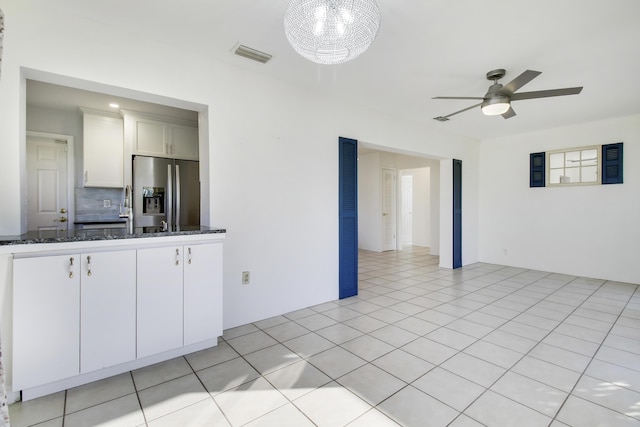 interior space featuring stainless steel refrigerator with ice dispenser, white cabinetry, light tile patterned floors, dark stone counters, and ceiling fan with notable chandelier