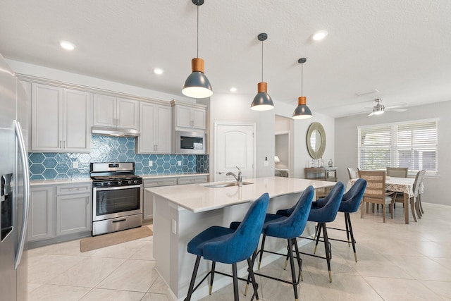 kitchen featuring gray cabinets, appliances with stainless steel finishes, sink, hanging light fixtures, and a center island with sink