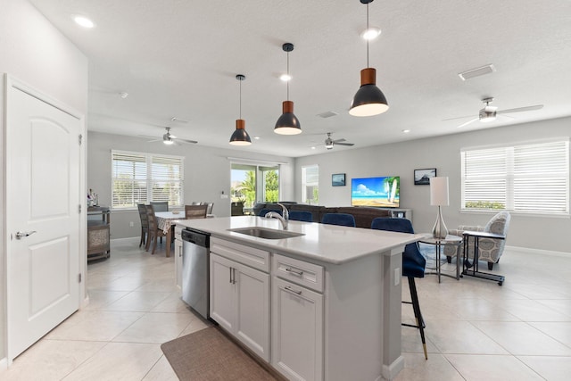 kitchen with sink, hanging light fixtures, light tile patterned floors, dishwasher, and a kitchen island with sink