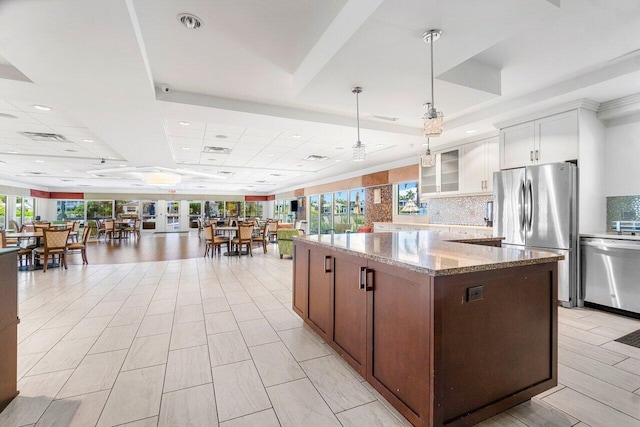 kitchen featuring hanging light fixtures, stainless steel appliances, light stone counters, a raised ceiling, and white cabinets