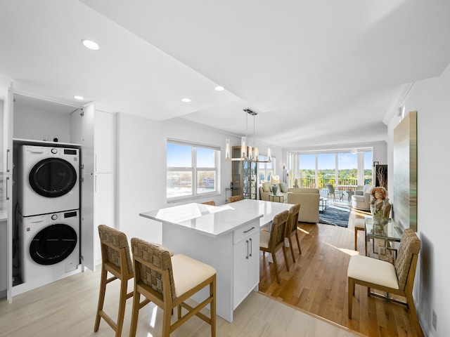 kitchen featuring white cabinetry, light hardwood / wood-style floors, a notable chandelier, stacked washer / dryer, and pendant lighting