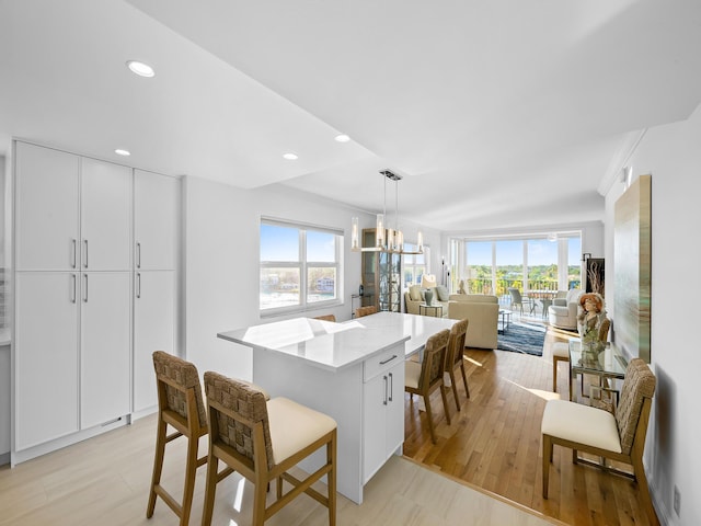 kitchen with light hardwood / wood-style flooring, hanging light fixtures, a notable chandelier, a kitchen island, and white cabinetry