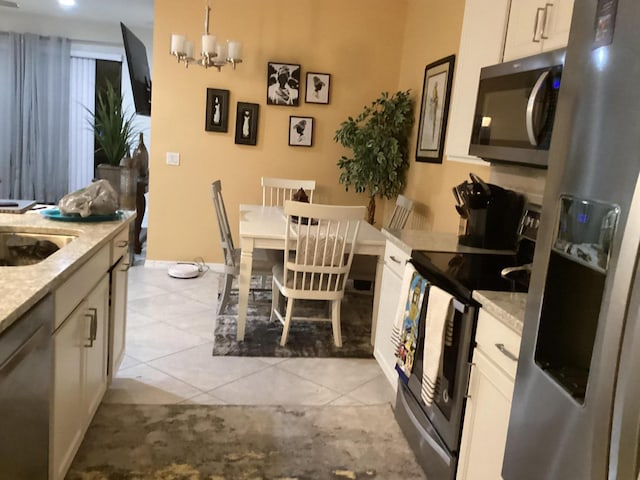 kitchen featuring stainless steel appliances, hanging light fixtures, light tile patterned floors, and light stone counters