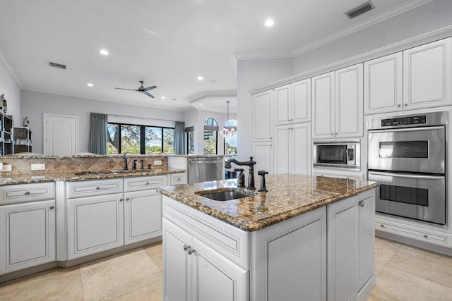 kitchen with sink, appliances with stainless steel finishes, stone counters, and a center island with sink