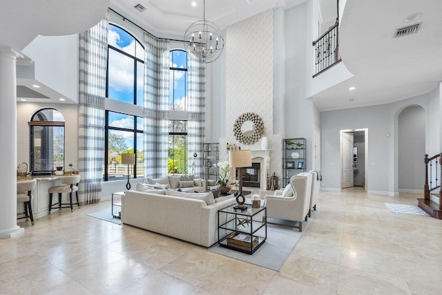 living room with ornate columns, an inviting chandelier, crown molding, a large fireplace, and a high ceiling