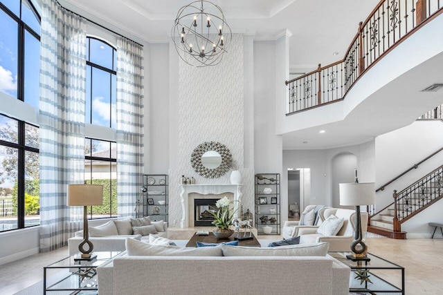 living room featuring a high ceiling, ornamental molding, a tray ceiling, a premium fireplace, and an inviting chandelier