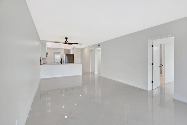 unfurnished living room featuring a ceiling fan and baseboards
