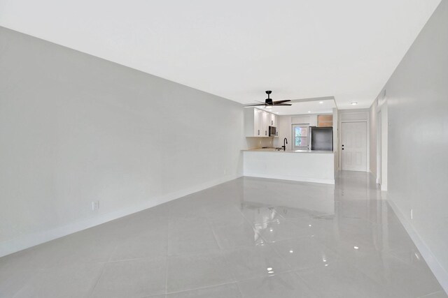 unfurnished living room with a ceiling fan, baseboards, and a sink