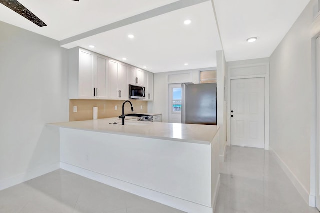 kitchen with light tile patterned floors, stainless steel appliances, kitchen peninsula, and white cabinets