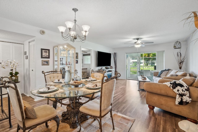 dining area with wood-type flooring, ceiling fan with notable chandelier, and a textured ceiling