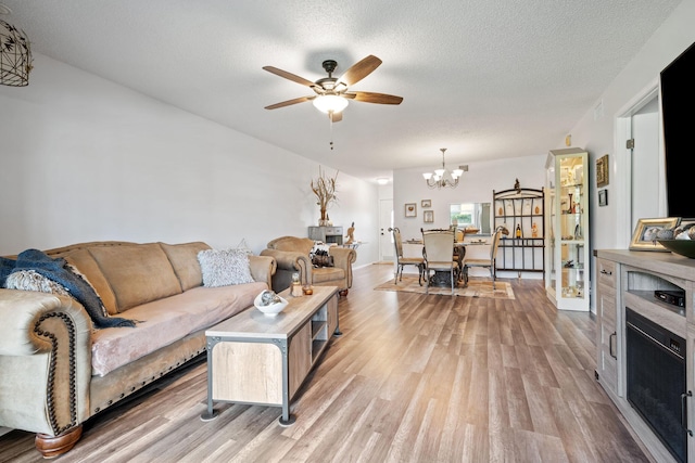 living room with ceiling fan with notable chandelier, light hardwood / wood-style floors, and a textured ceiling