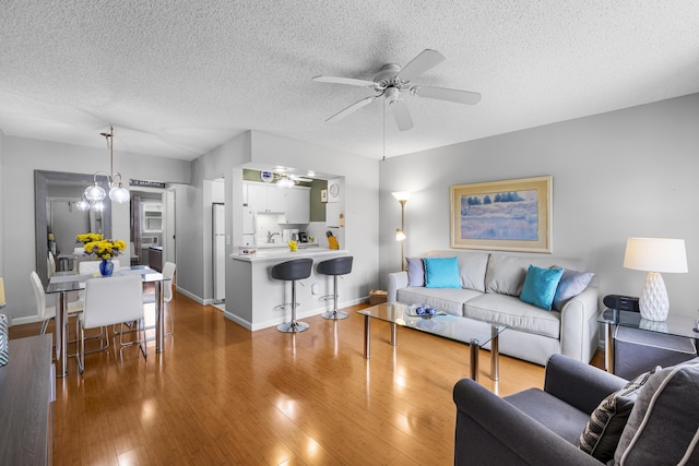 living room featuring wood-type flooring, ceiling fan with notable chandelier, and a textured ceiling