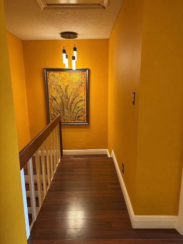 hall featuring dark wood-type flooring, an inviting chandelier, and a textured ceiling