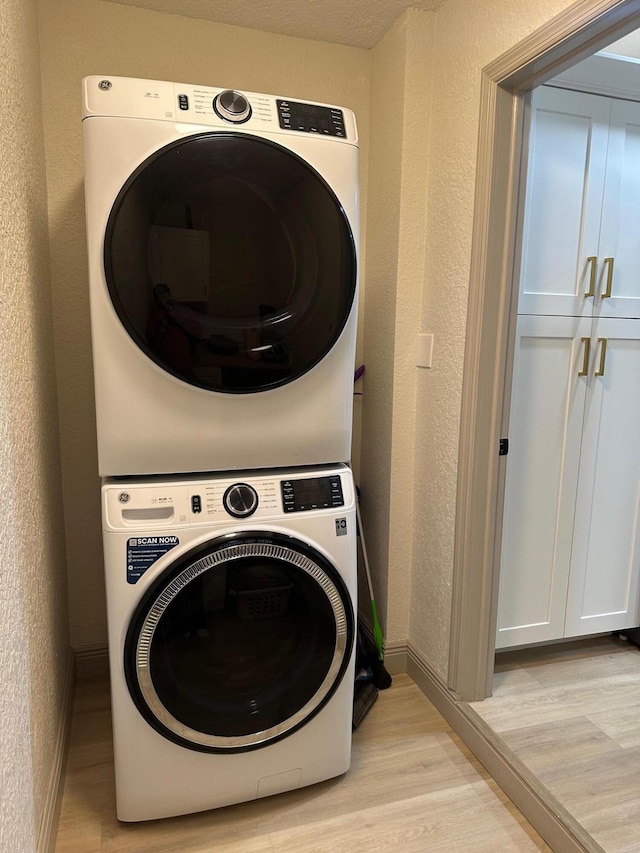 laundry room with light hardwood / wood-style floors, cabinets, and stacked washing maching and dryer