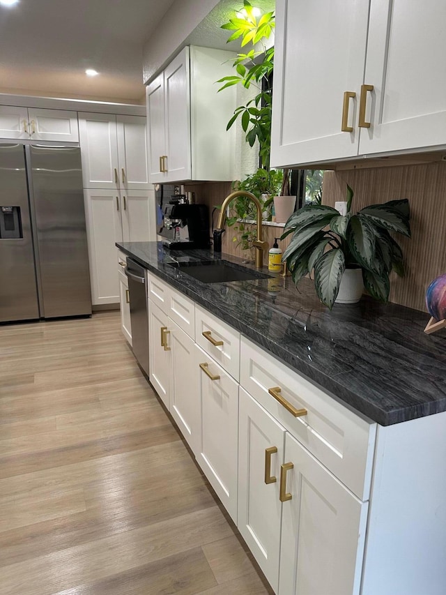 kitchen with sink, appliances with stainless steel finishes, white cabinets, dark stone counters, and light wood-type flooring