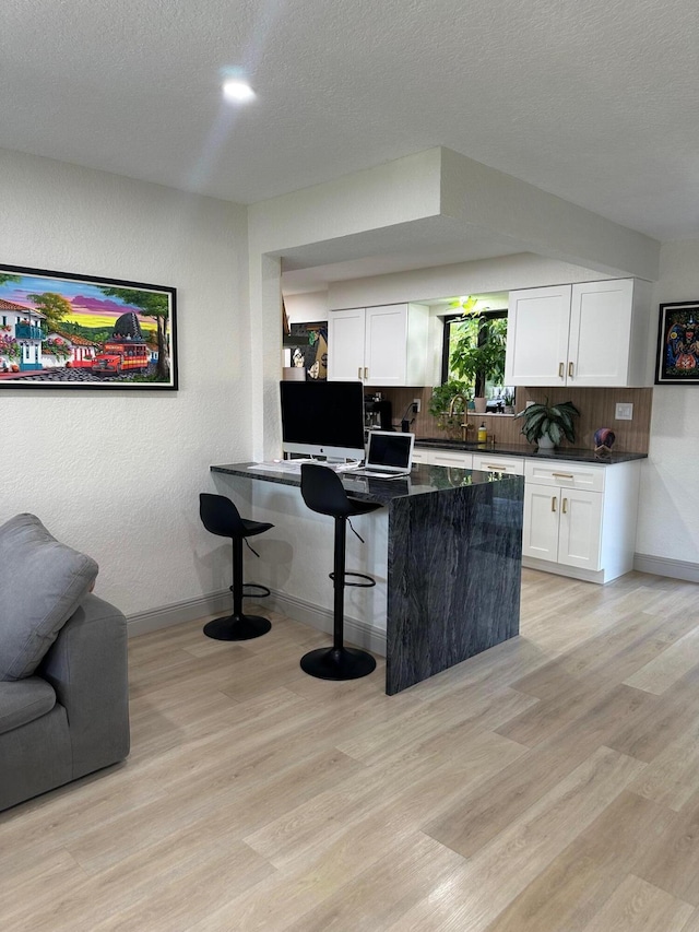 kitchen with backsplash, a textured ceiling, a kitchen bar, white cabinets, and light wood-type flooring