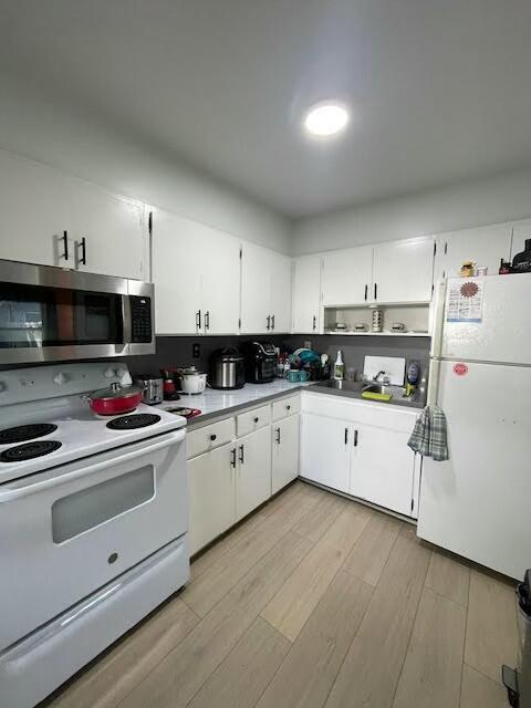 kitchen with white cabinetry, backsplash, white appliances, and light hardwood / wood-style floors