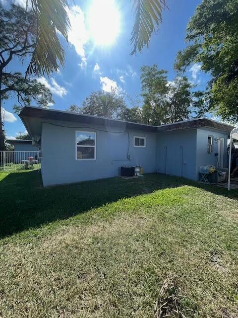 back of house with cooling unit and a lawn