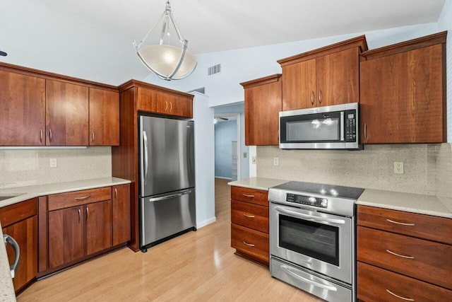 kitchen featuring backsplash, decorative light fixtures, light wood-type flooring, and appliances with stainless steel finishes