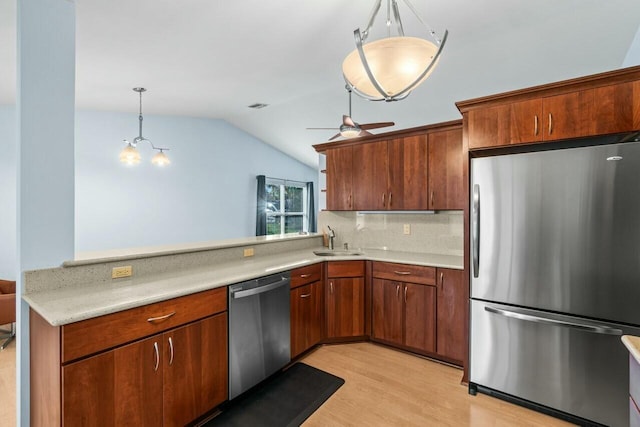 kitchen featuring vaulted ceiling, appliances with stainless steel finishes, pendant lighting, light hardwood / wood-style floors, and kitchen peninsula