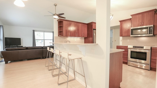 kitchen with light hardwood / wood-style flooring, ceiling fan, appliances with stainless steel finishes, a kitchen breakfast bar, and vaulted ceiling