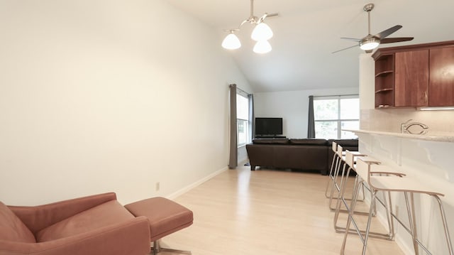 living room with sink, ceiling fan with notable chandelier, vaulted ceiling, and light wood-type flooring