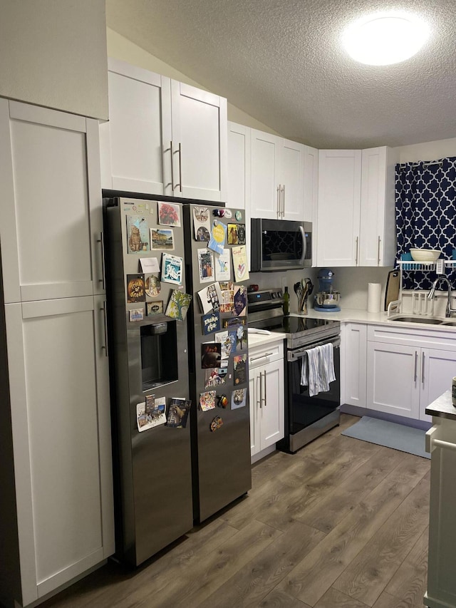 kitchen with appliances with stainless steel finishes, a textured ceiling, white cabinets, sink, and dark hardwood / wood-style floors