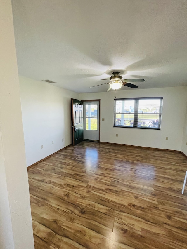 unfurnished room with a healthy amount of sunlight, ceiling fan, baseboards, and wood finished floors