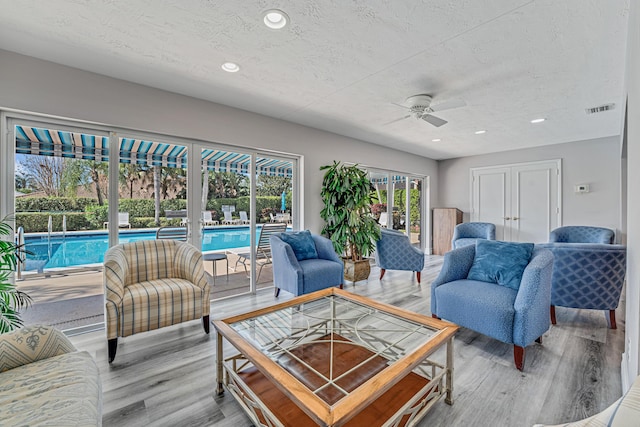 living room featuring hardwood / wood-style flooring, ceiling fan, and a textured ceiling