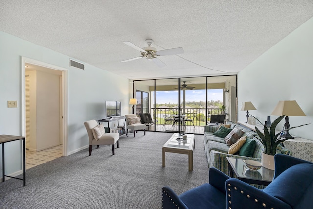 carpeted living room featuring visible vents, a ceiling fan, a textured ceiling, a wall of windows, and baseboards