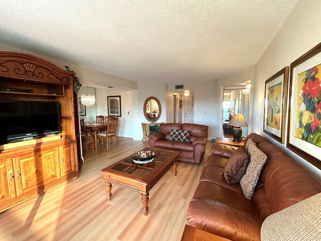 living room with an inviting chandelier, light hardwood / wood-style floors, and a textured ceiling