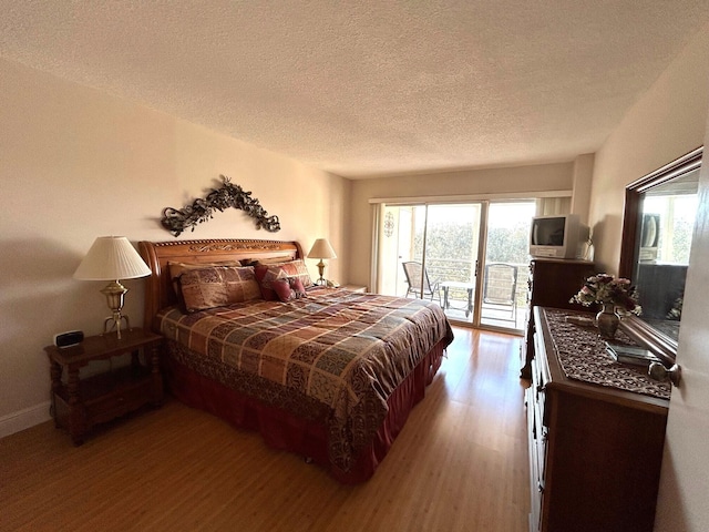 bedroom with hardwood / wood-style floors, access to exterior, and a textured ceiling