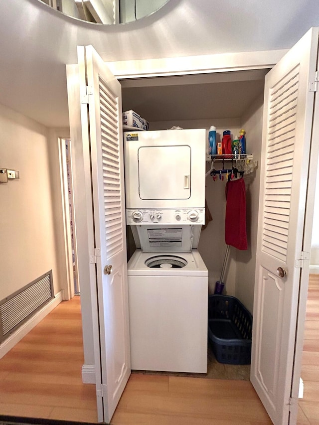 laundry room with stacked washing maching and dryer and light hardwood / wood-style flooring