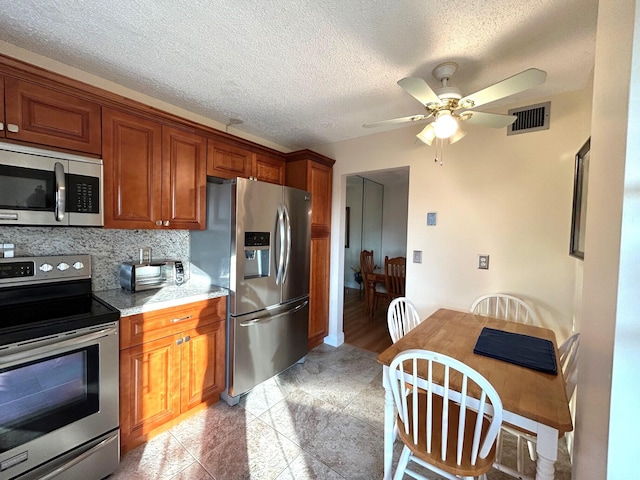 kitchen featuring appliances with stainless steel finishes, decorative backsplash, light stone counters, ceiling fan, and a textured ceiling