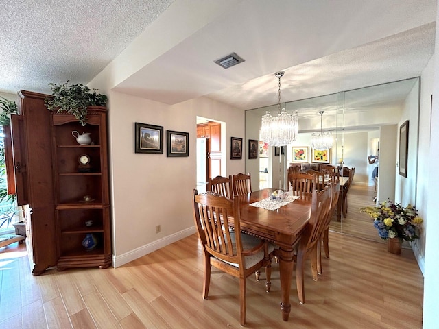 dining room with a notable chandelier, a textured ceiling, and light wood-type flooring