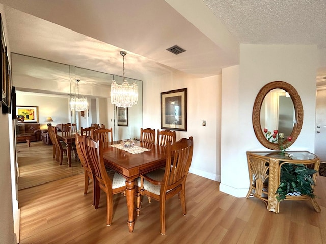 dining area with a textured ceiling, a notable chandelier, and light hardwood / wood-style floors