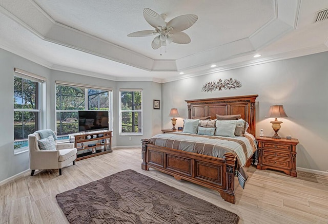 bedroom featuring crown molding, ceiling fan, light wood-type flooring, and a tray ceiling