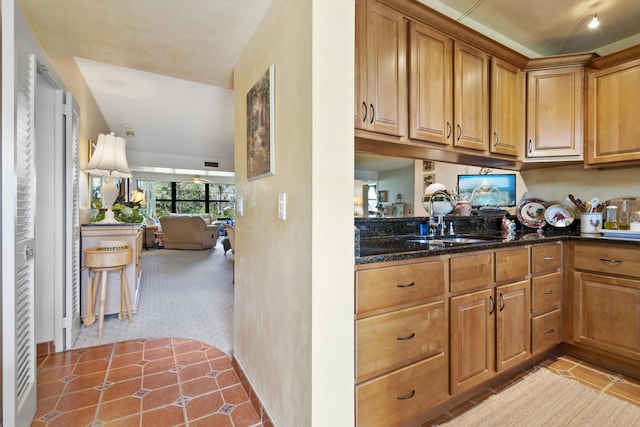 kitchen with dark stone counters, sink, and light carpet