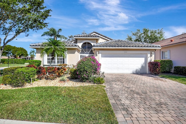 view of front of home featuring stucco siding, a tiled roof, an attached garage, decorative driveway, and a front yard