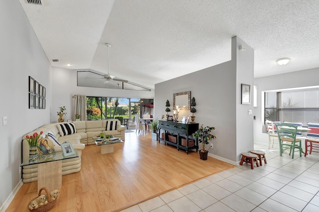 living room with light tile patterned flooring, vaulted ceiling, ceiling fan, and a textured ceiling