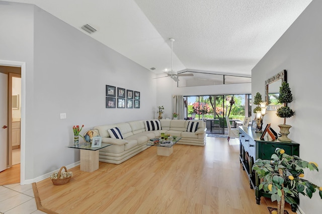 living room featuring a textured ceiling, vaulted ceiling, light hardwood / wood-style floors, and ceiling fan