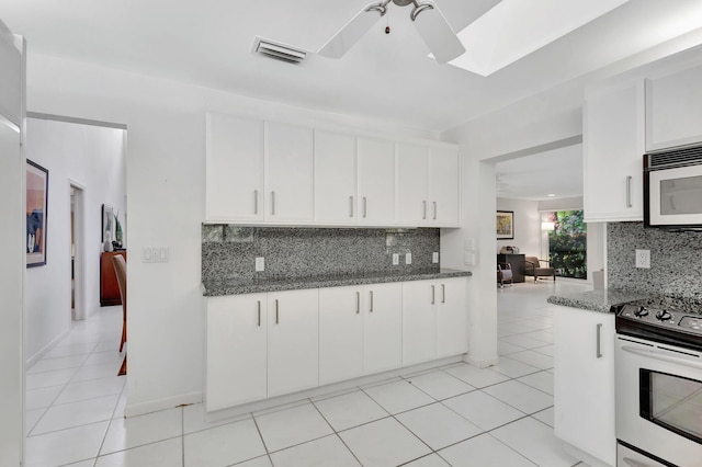 kitchen with light tile patterned flooring, dark stone countertops, white cabinets, backsplash, and stainless steel range with electric stovetop