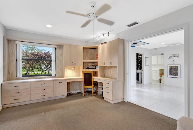 carpeted office space with built in desk and ceiling fan