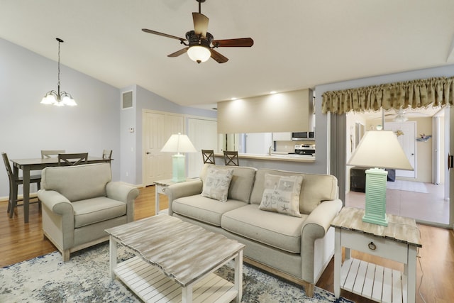 living room with lofted ceiling, ceiling fan with notable chandelier, and light wood-type flooring